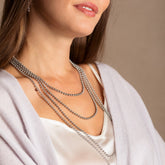A model wearing four silver chains in varying lengths from a short, 16-inch silver chain to a 36-inch silver chain with matching silver earrings in the same iconic chain design. All hand-crafted Italian jewelry is made by DelBrenna Italian Jewelers in Tuscany.